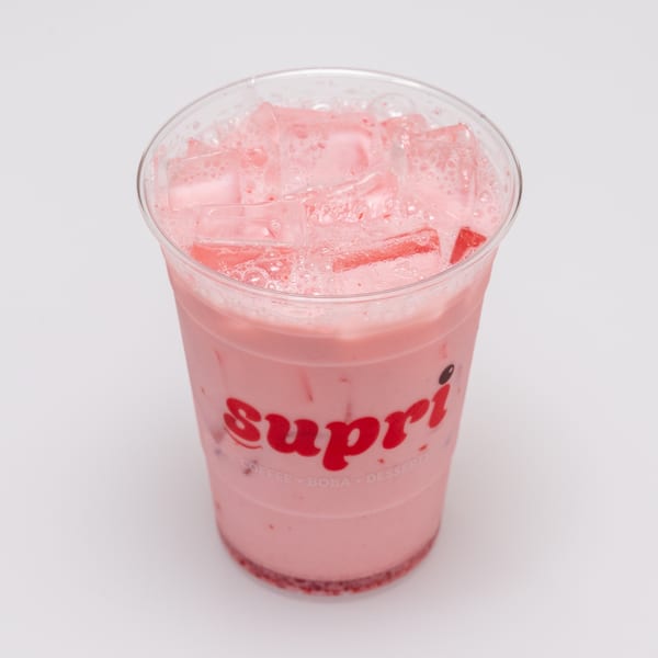 A clear plastic cup of pink strawberry milk tea with ice and a red "Supri" logo.