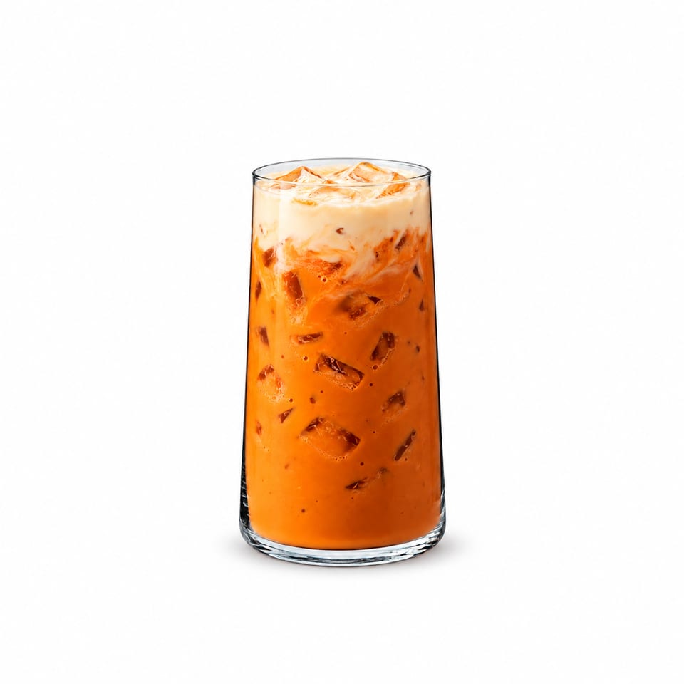 Tall glass of creamy orange iced tea filled with ice cubes against a white background.